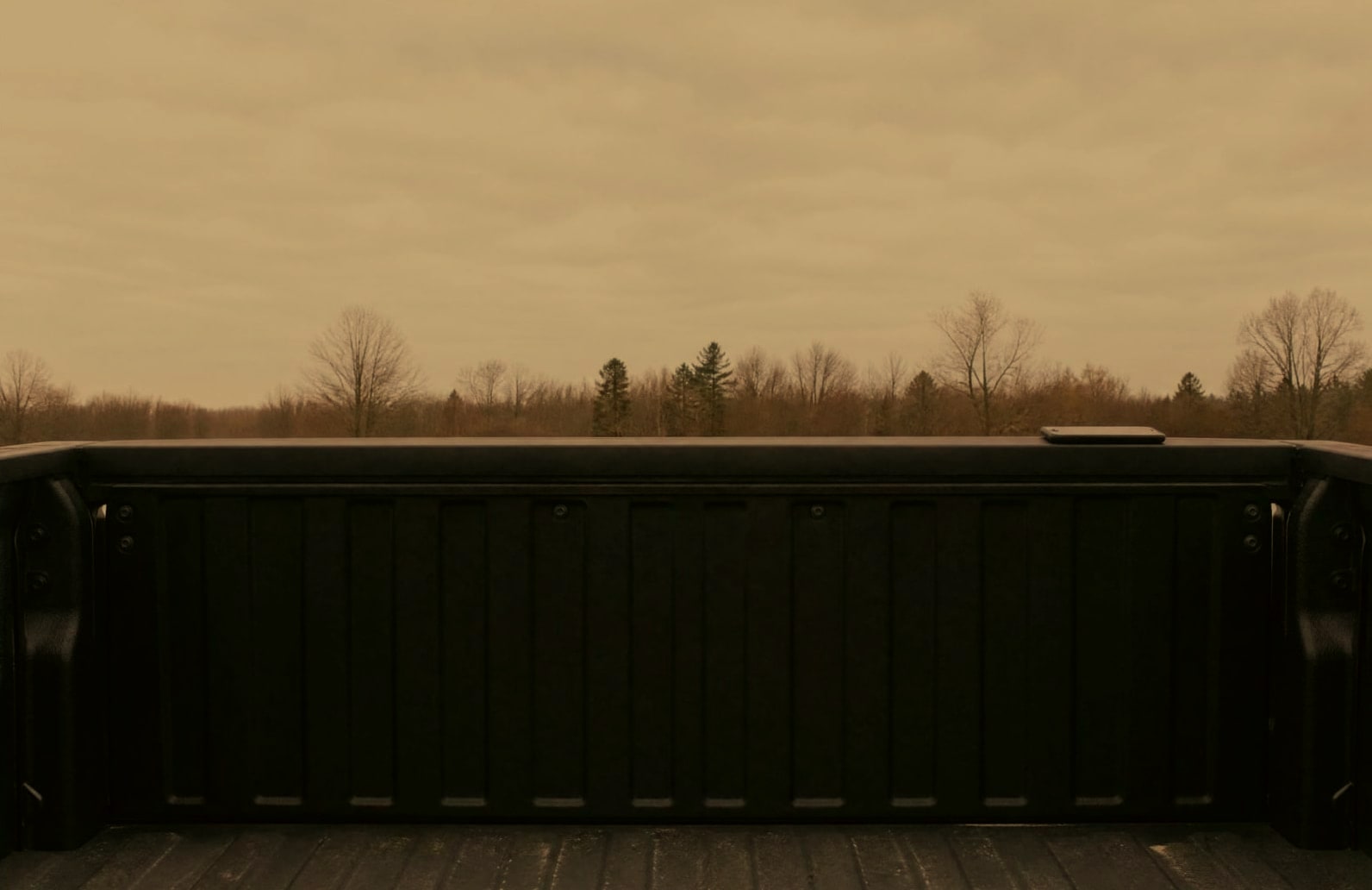A phone lying face-down on a pickup tailgate under an overcast sky.